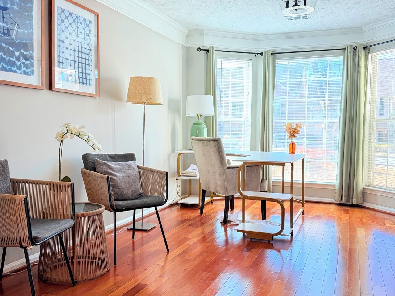 A room with a wooden floor, a dining table with chairs, a lamp, and framed artwork on the wall.