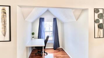 Un pequeño cuarto ático triangular con escritorio, silla y ventana con cortinas.