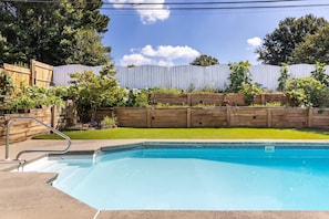 A backyard with a swimming pool, wooden fence, and greenery.
