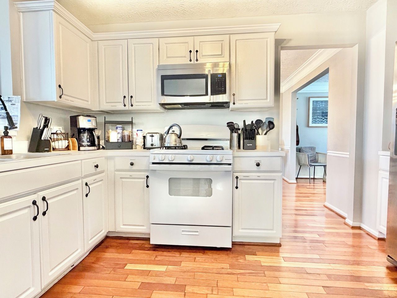 A kitchen with white cabinetry, a stainless steel microwave, a stove, and a toaster.