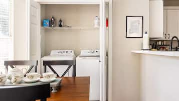 Cocina compacta con lavadora, una mesita con juego de té y un certificado enmarcado en la pared.