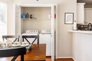 A compact kitchen with a washing machine, a small table with tea set, and a framed certificate on the wall.