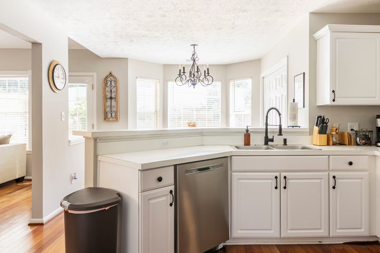 A modern kitchen with white cabinetry, a stainless steel dishwasher, and a chandelier.