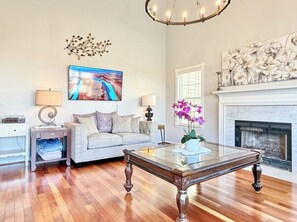 A living room with a sofa, a glass coffee table, a fireplace, and a painting on the wall.