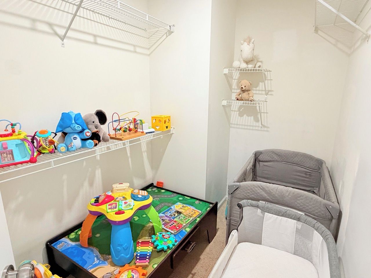 A child's play area with toys and a play mat, a crib, and a shelf with stuffed animals.