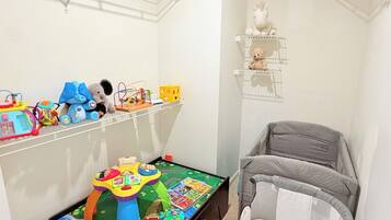 A child's play area with toys and a play mat, a crib, and a shelf with stuffed animals.