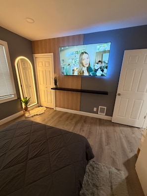 A bedroom with a bed, a television mounted on the wall, and a door.