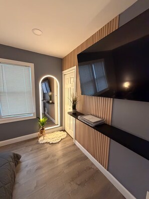 A modern interior with a wooden floor, a TV mounted on a wall, and a hallway leading to a door.
