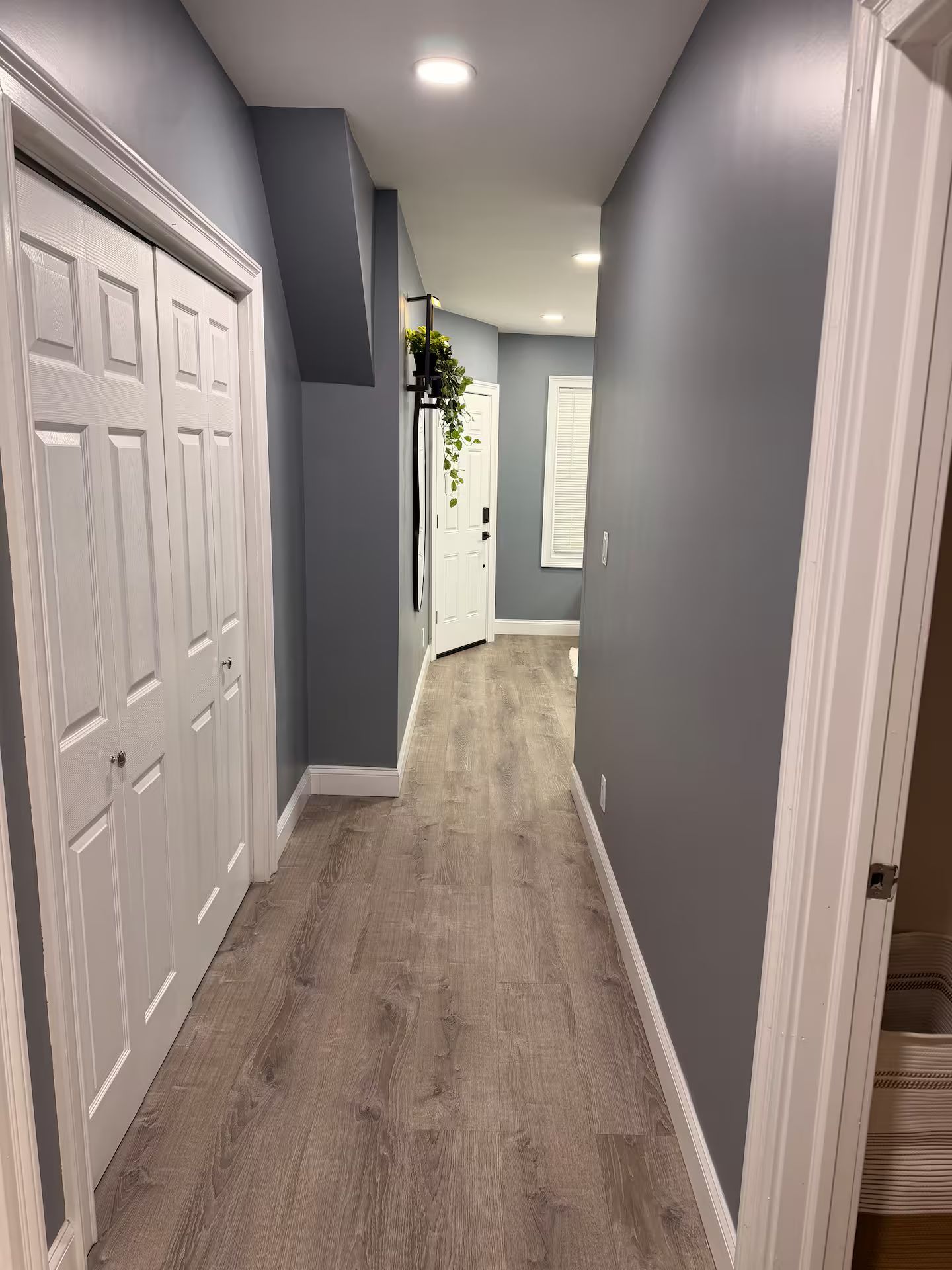 Un couloir avec un plancher en bois, des murs gris et des portes blanches.