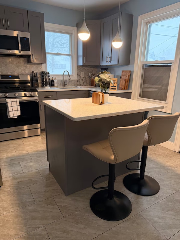A modern kitchen with a central island, bar stools, stainless steel appliances, and pendant lighting.