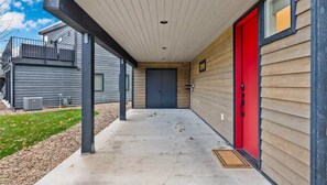 A covered walkway leading to a building with a red door and a grey door, with a metal railing on the left and a wooden wall on the right. - Entire Home in Whitefish, Montana (Whitefish)