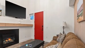 A living room with a fireplace, a red door, a television, and a couch. - Entire Home in Whitefish, Montana (Whitefish)