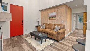 A modern living room with a red door, a brown leather sofa, a black ottoman, and a wooden wall panel. - Entire Home in Whitefish, Montana (Whitefish)