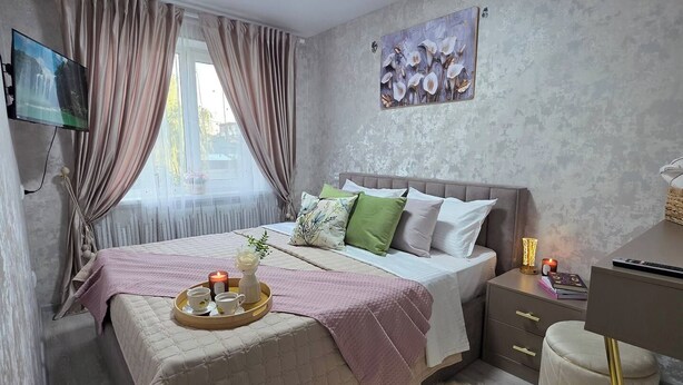 Een slaapkamer met een bed, nachtkastje, lamp en een schilderij aan de muur.