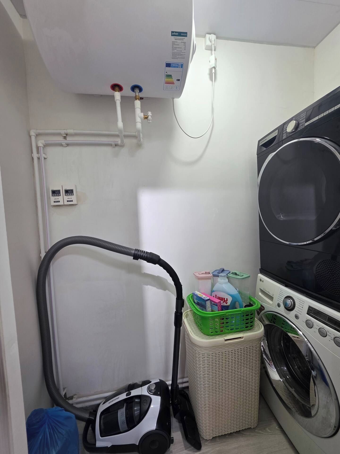 A laundry room with a washing machine, a vacuum cleaner, and a utility meter.