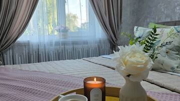 A cozy bedroom with a bed, a bedside table with a candle, and a tray with two cups of tea.