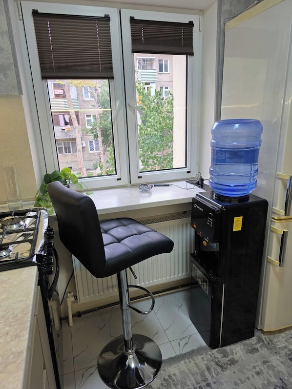 A kitchen with a gas stove, a black bar stool, a water dispenser, and a view of buildings through the window.