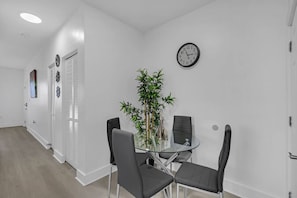 Ein modernes Interieur mit einem Glastisch und Stühlen, einer Uhr an der Wand und einer Bambuspflanze.
