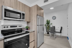 Eine moderne Küche mit Mikrowelle, Backofen und Kühlschrank, ein Essbereich mit Stühlen und einem Tisch sowie eine Uhr an der Wand.