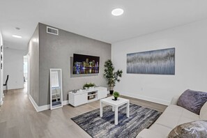 Ein modernes Wohnzimmer mit einem Flachbildfernseher, einem großen abstrakten Gemälde, einem weißen Sofa und einem Couchtisch.