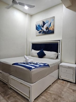 Ein Schlafzimmer mit einem Bett, einem Nachttisch, einem Deckenventilator und einem Wandbild.