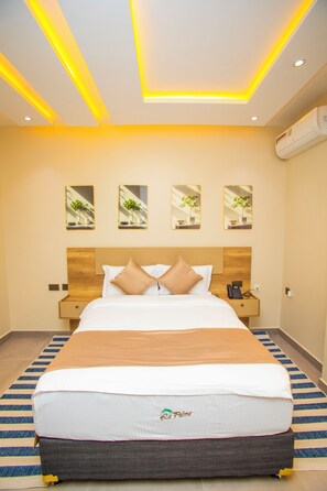 A hotel room with a large bed, bedside tables, a phone, and wall-mounted air conditioning.