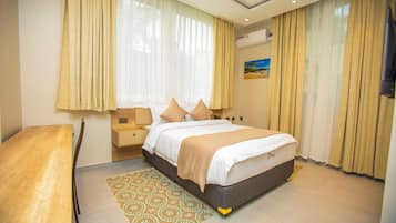 A hotel room with a bed, bedside table, nightstand, and a patterned rug.