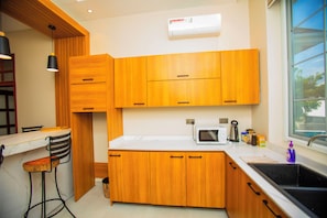 Cocina moderna con armarios de madera, encimera blanca, microondas, lavamanos y ventana con vistas al exterior.