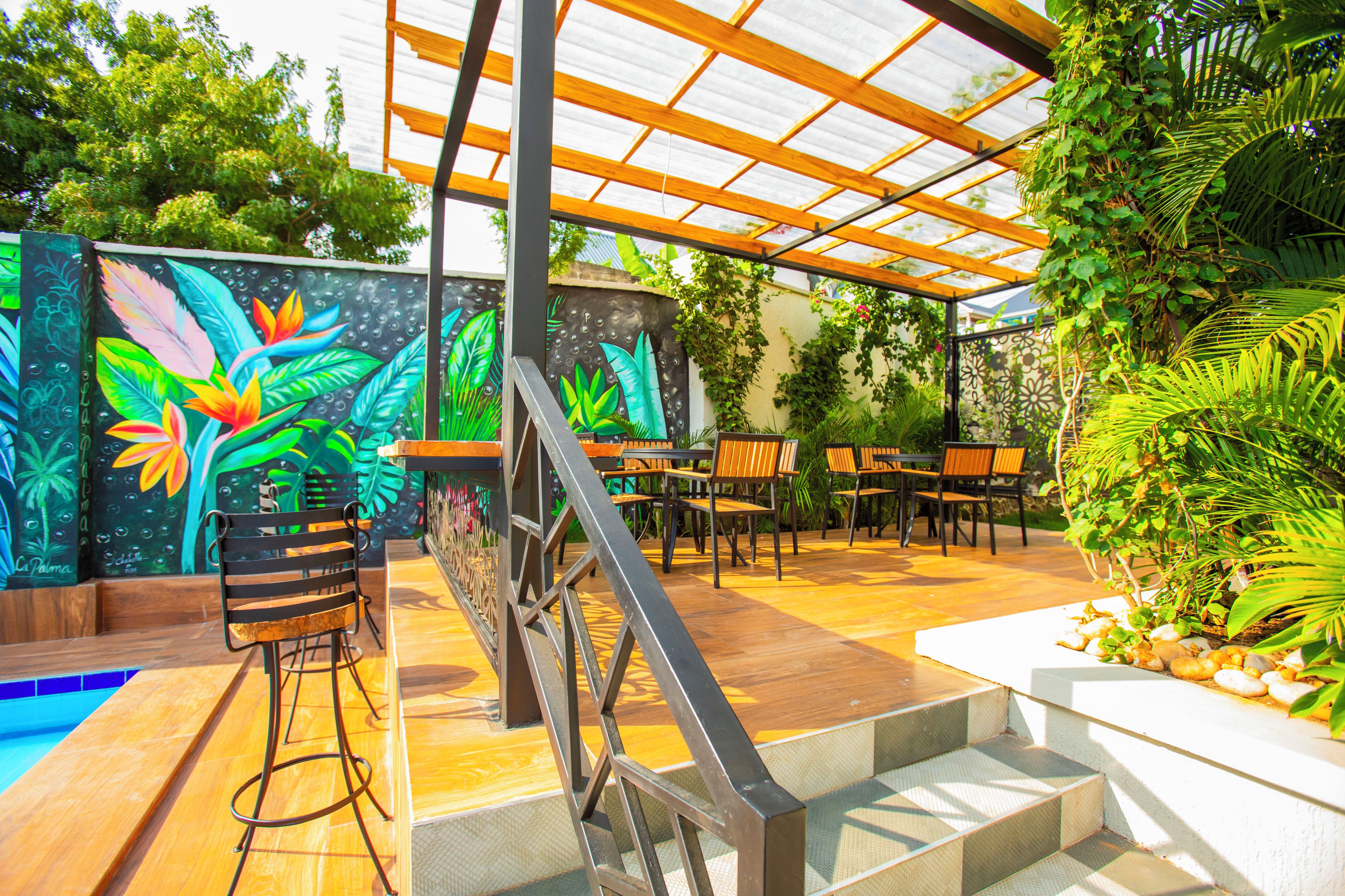 Un espacio de estar al aire libre cubierto con piscina, rodeado de abundante vegetación y un mural vibrante.