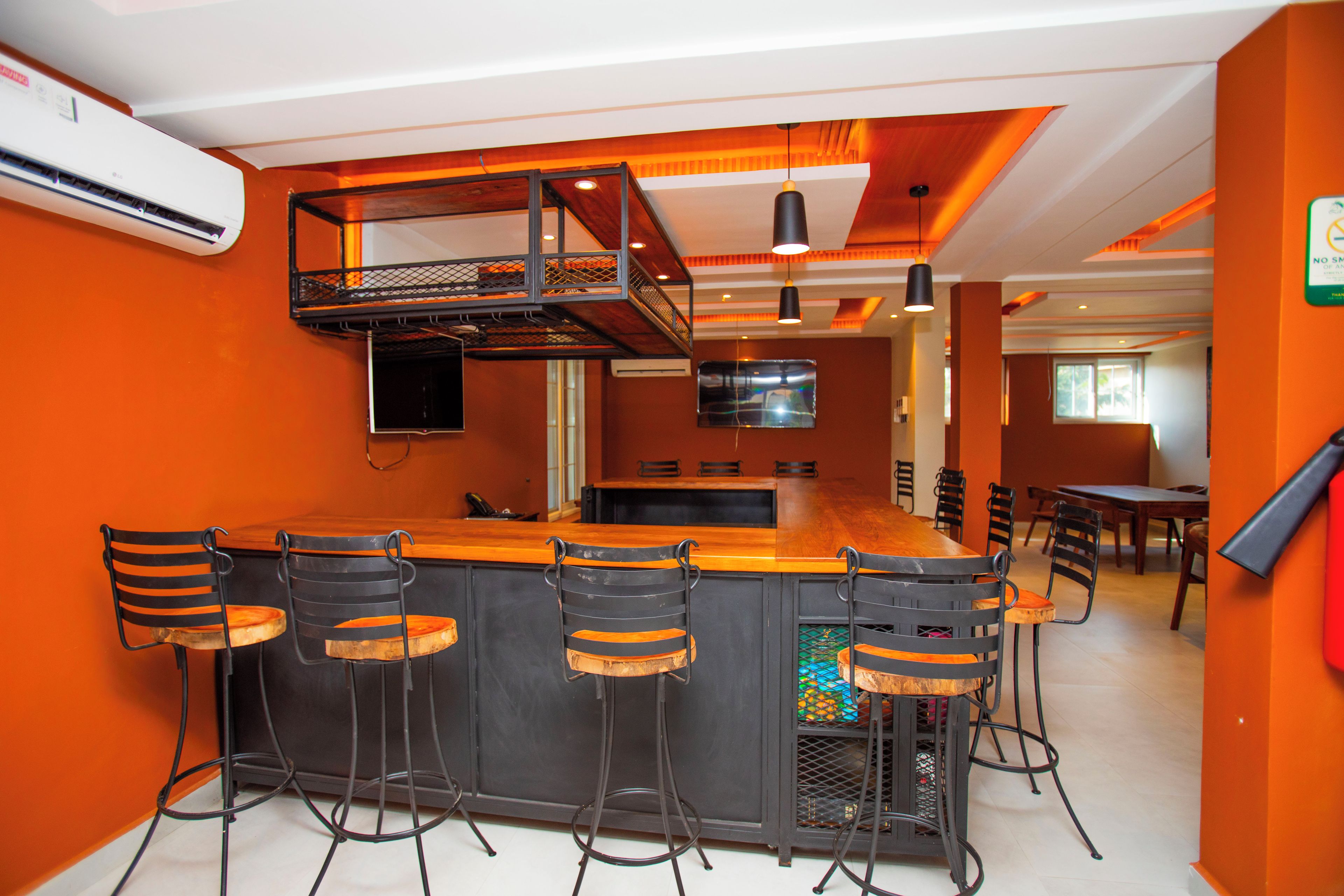 Zona de bar con una barra alta y varios taburetes, una cocina al fondo y un comedor con sillas.