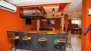 Zona de bar con una barra alta y varios taburetes, una cocina al fondo y un comedor con sillas.