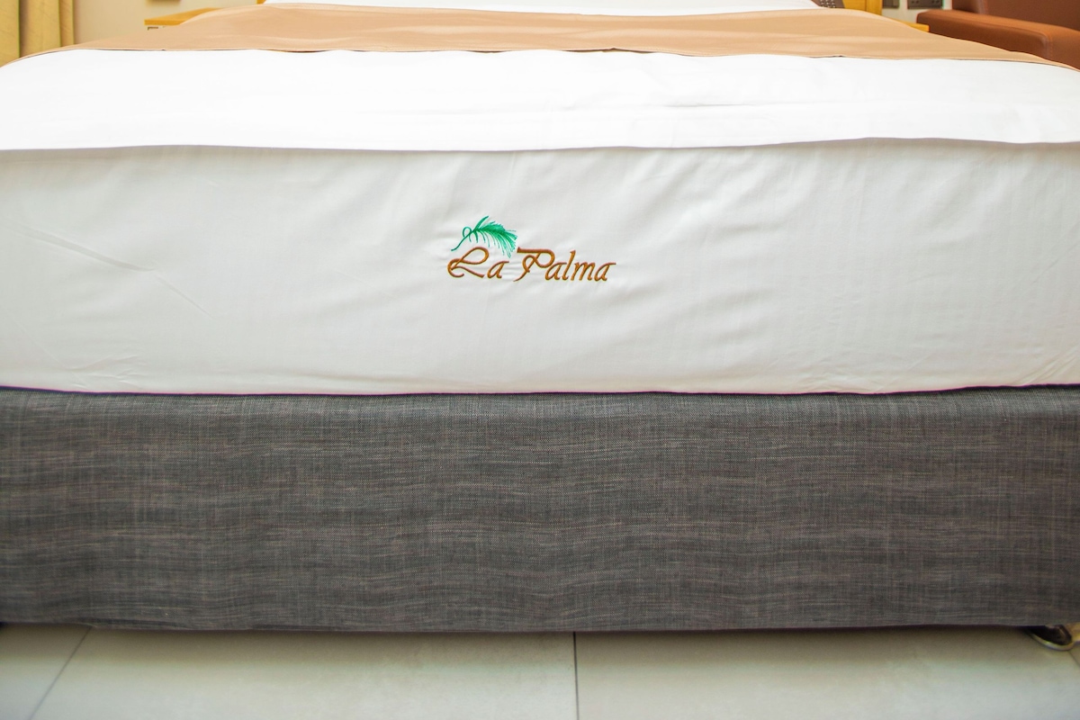 Una habitación de hotel con una cama grande, un cabecero, un cuadro en la pared y una lámpara en el techo.