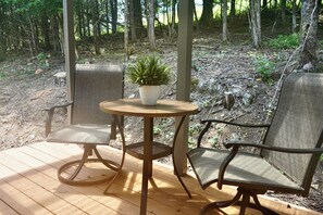 Een terras met een ronde tafel en twee stoelen, omgeven door bebossing.