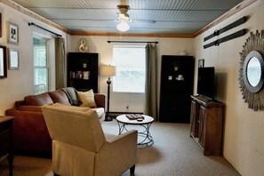 Ein gemütliches Wohnzimmer mit Ledersofa, einem kleinen runden Couchtisch und einem Fernseher auf einer Holzkommode.