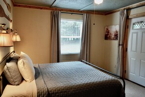 Een slaapkamer met een bed, een raam met gordijnen, een deur en wandlampen.