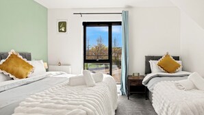 Ein modernes Schlafzimmer mit zwei Betten, Blick ins Freie und einem kleinen Tisch mit einer Uhr.