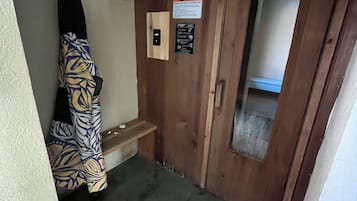 A small room with a wooden door, a bench, a towel rack, and a warning sign.