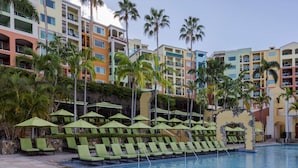 Zona de piscina de hotel con múltiples sillones de descanso y sombrillas, rodeada de edificios de varios pisos con balcones.