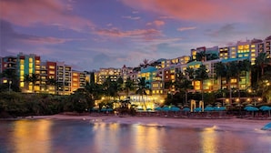 Un hotel frente a la playa con varias edificaciones, una playa de arena y palmeras.