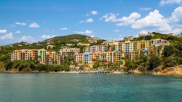 Un hotel frente al mar con varios edificios de colores, una vista despejada y un paisaje montañoso de fondo.