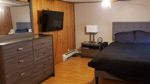 Une chambre à coucher comprenant un lit, une commode, une table de chevet, une lampe et un téléviseur.