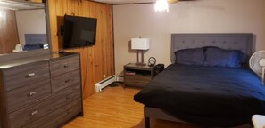 Ett sovrum med en säng, byrå, sängbord, lampa och en tv.