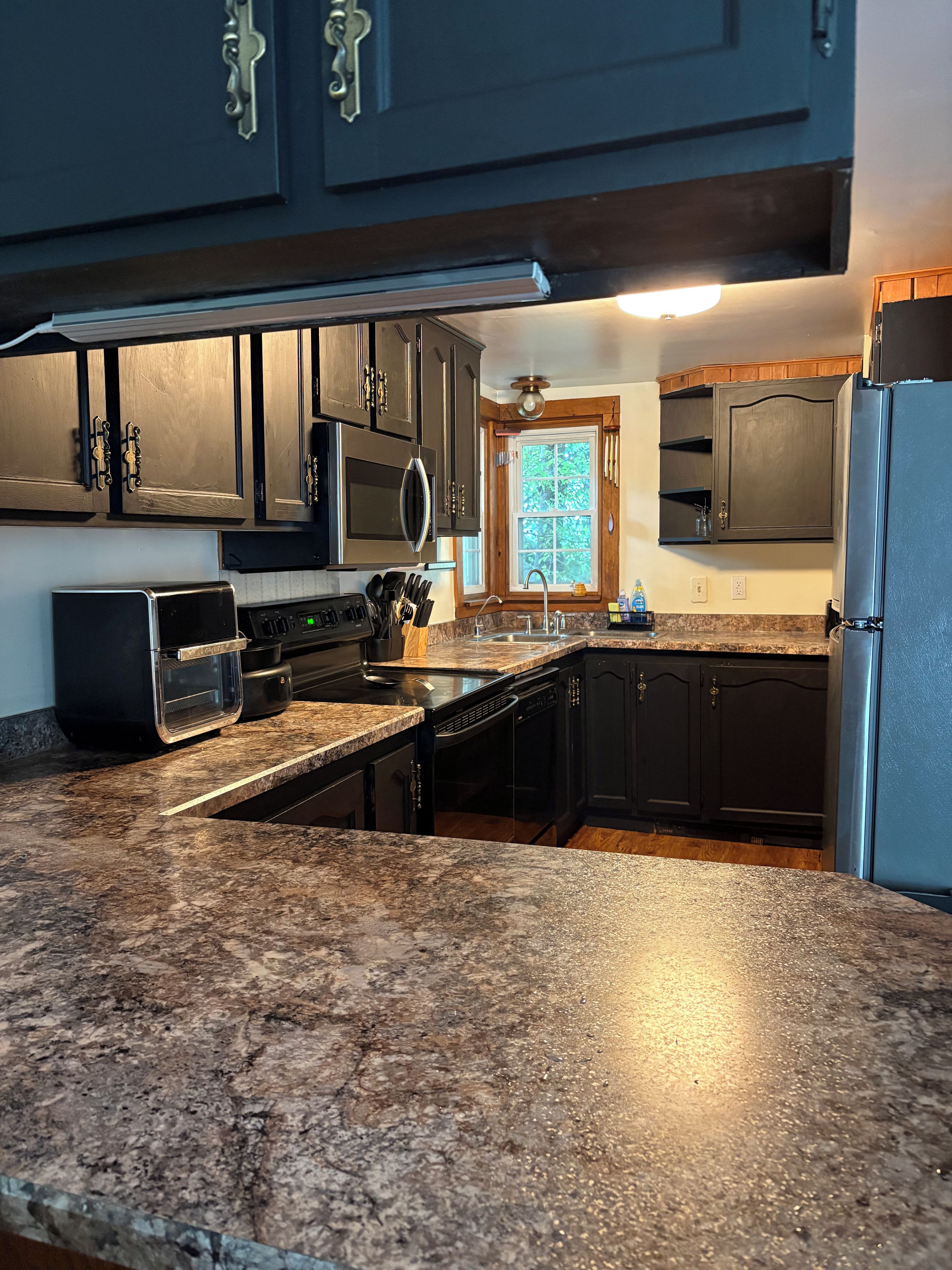 A kitchen with dark wooden cabinets, a granite countertop, a built-in microwave, and a stainless steel refrigerator.