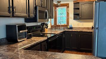 A kitchen with dark wooden cabinets, a granite countertop, a built-in microwave, and a stainless steel refrigerator.