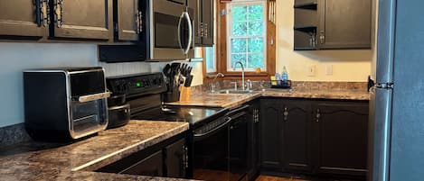 A kitchen with dark wooden cabinets, a granite countertop, a built-in microwave, and a stainless steel refrigerator.