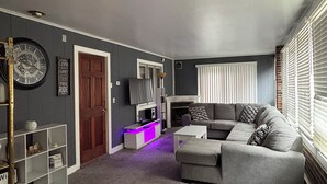 Un salon avec un canapé gris, une table basse blanche et une cheminée. On y trouve une porte en bois et une étagère blanche.