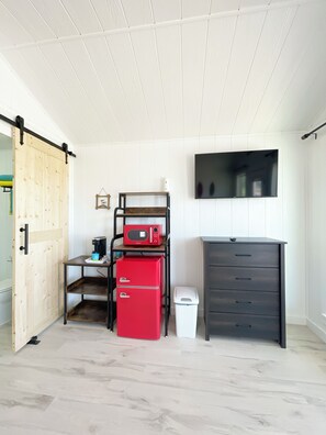 A compact kitchen with a sliding door, a microwave, a red mini-fridge, a white trash bin, and a dark wooden cabinet. - Sunrise Yellow Cabin #5 Quitman, Tx (Quitman)