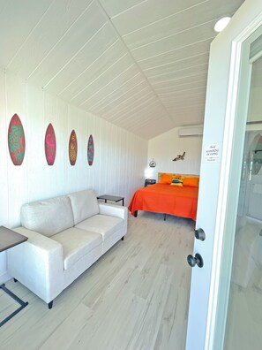 A room with a white sofa, a bed with an orange bedspread, and a wall with surfboard decorations. - Sunrise Yellow Cabin #5 Quitman, Tx (Quitman)