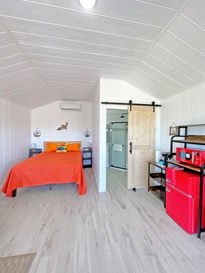 A bedroom with a bed, a red appliance, and a sliding door leading to a bathroom. - Sunrise Yellow Cabin #5 Quitman, Tx (Quitman)