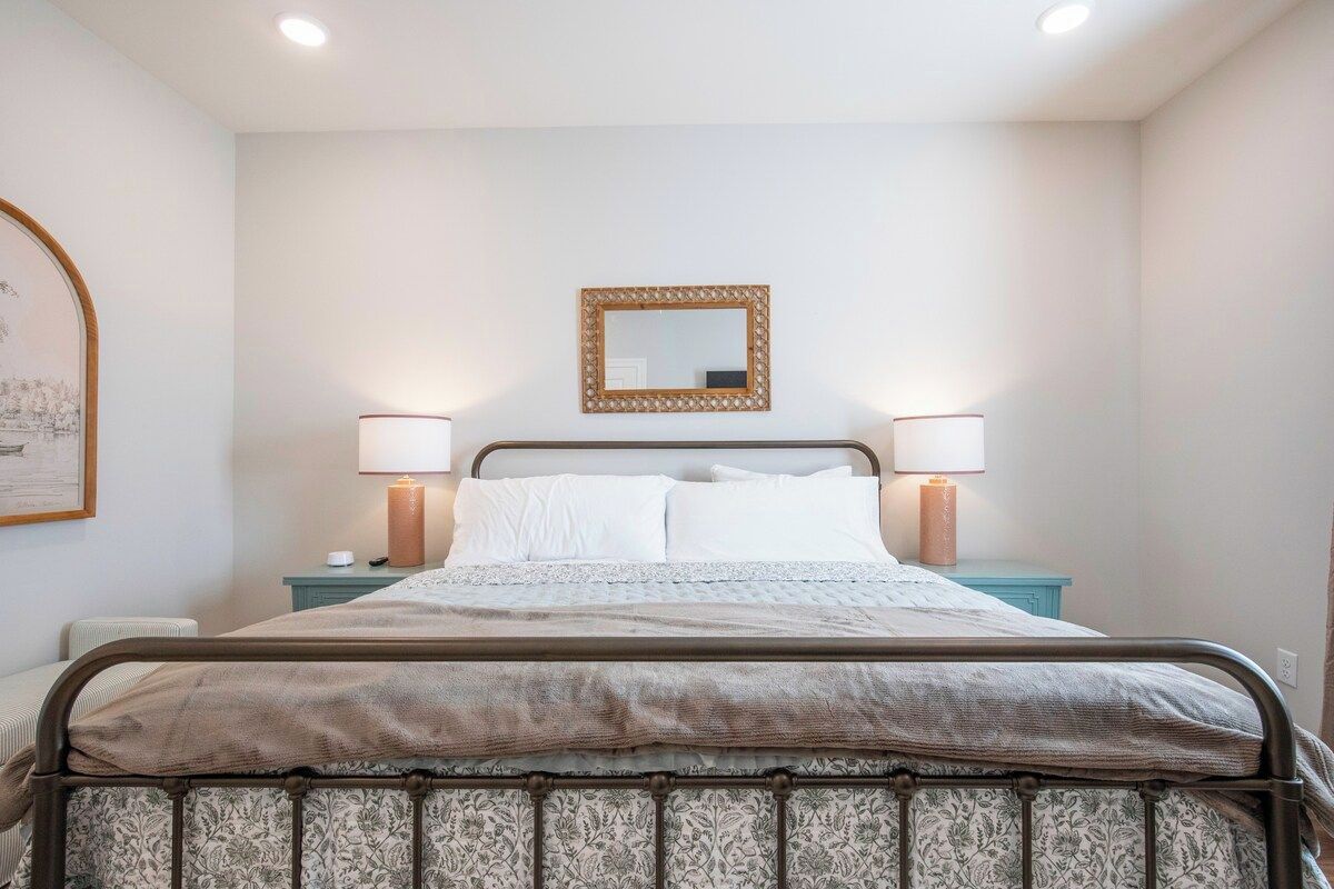 A bed with a metal frame, two bedside lamps, a mirror above the bed, and a wall-mounted picture frame.